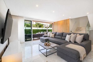 A modern living room with a large grey sofa, a flat-screen TV, and a glass coffee table.