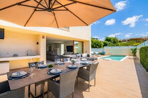 An outdoor dining area with a table set for four, a pool, and a view of the surrounding landscape.