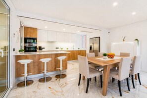 A modern kitchen with a central island, bar stools, and a dining table with chairs.