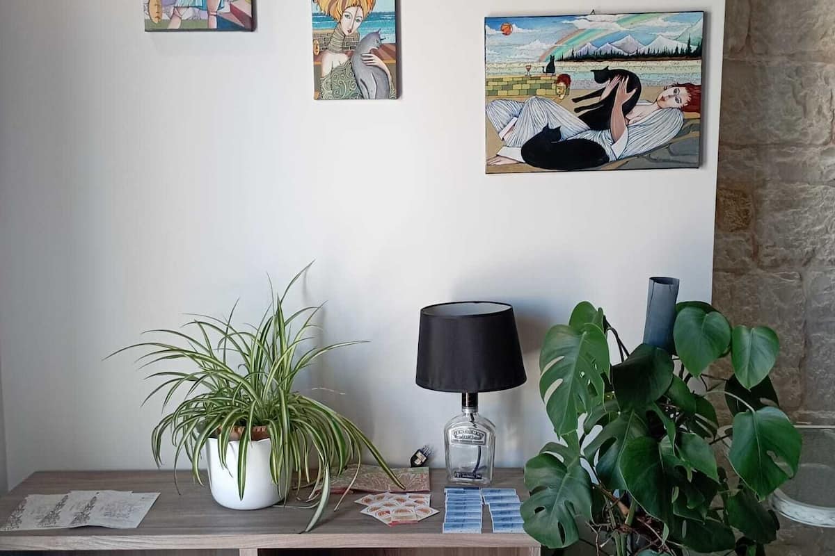 A room with a wooden desk, a potted plant, a clock, and four framed artworks on the wall.