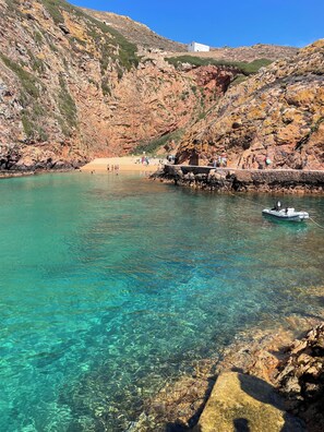 A coastal area with clear turquoise water, rocky cliffs, and a small boat anchored near the shore.