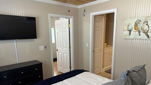 A bedroom with a bed, a dresser, a television, and a door leading to another room.