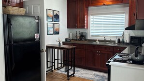 A kitchen with wooden cabinets, a black refrigerator, a stove, and a window with blinds.