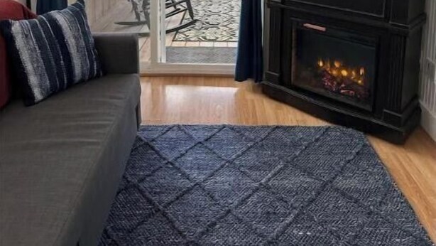 A living room with a fireplace, a television mounted on the wall displaying streaming services, a sliding glass door leading to a patio, and a couch with a patterned rug.