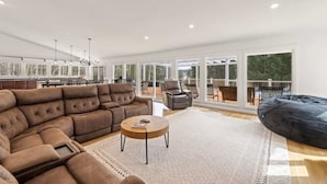 A spacious living area with a sectional sofa, a round coffee table, and a bean bag. - Luxury 5b 3ba on 10 acres w Lake view, Firepit, Hot Tub, Gameroom, close to Ski! (Sanbornton)
