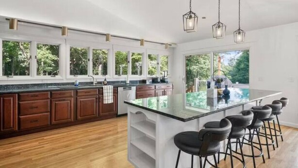A modern kitchen with wooden cabinets, a large island with bar stools, and pendant lighting. - Luxury 5b 3ba on 10 acres w Lake view, Firepit, Hot Tub, Gameroom, close to Ski! (Sanbornton)