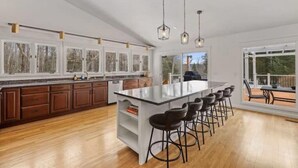 A spacious kitchen with a large island, wooden cabinets, and a bar area with stools. - Luxury 5b 3ba on 10 acres w Lake view, Firepit, Hot Tub, Gameroom, close to Ski! (Sanbornton)