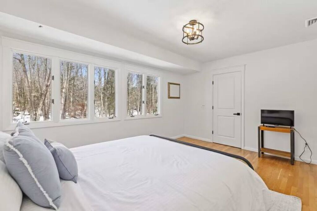 A bedroom with a large bed, a TV on a stand, and a window with a view of trees.