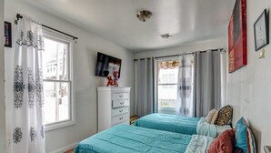 Une chambre avec deux lits, des murs blancs, un téléviseur à écran plat et une fenêtre agrémentée de rideaux à motifs.