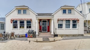 Une maison à deux étages avec une porte d’entrée rouge, un revêtement extérieur blanc et un petit porche aménagé avec du mobilier d’extérieur.