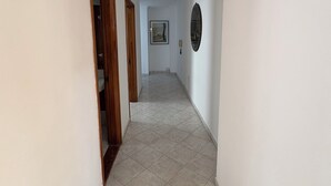 Un pasillo con paredes blancas, piso de baldosas y puertas de madera.