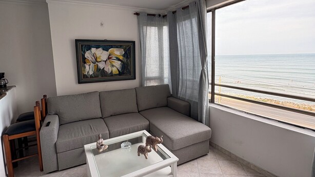 Una sala de estar con un sofá gris, una mesa de centro de vidrio y un cuadro en la pared.