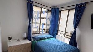 Un dormitorio con cama, mesita de noche, lámpara y cortinas.