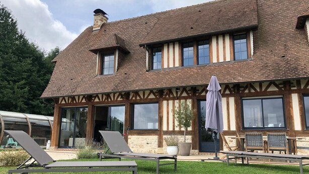 Une maison traditionnelle à colombages, dotée d’une grande pelouse à l’avant, d’un espace extérieur aménagé pour s’asseoir et d’un patio couvert.