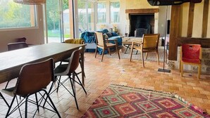 Un vaste espace de vie doté d’un plafond en bois, d’une cheminée et d’une grande fenêtre donnant sur un jardin.