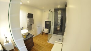 A modern bathroom with a glass shower enclosure, a white sink, and a wooden floor.