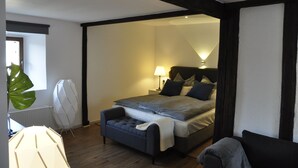 A modern bedroom with a bed, bedside table, lamp, and a large plant.