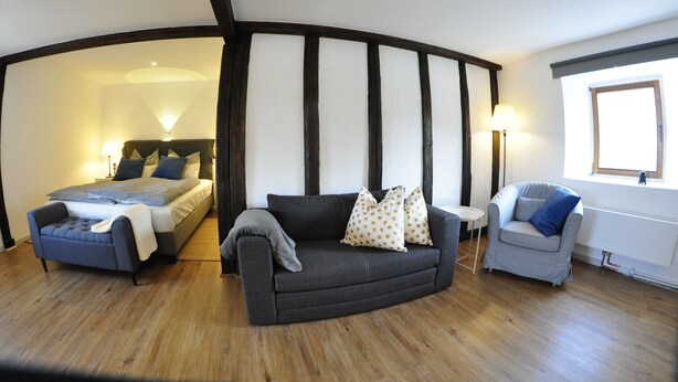 A room with a bed, a sofa, and a chair. There is a window and a lamp.