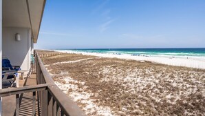 A balcony overlooking a beach with a sandy dune and ocean view.