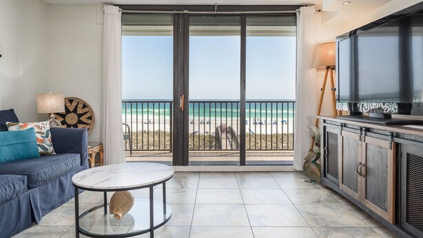 A balcony with a view of the beach, a sofa, a table, and a TV.