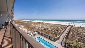 A balcony with a pool, beach view, and a wooden walkway.