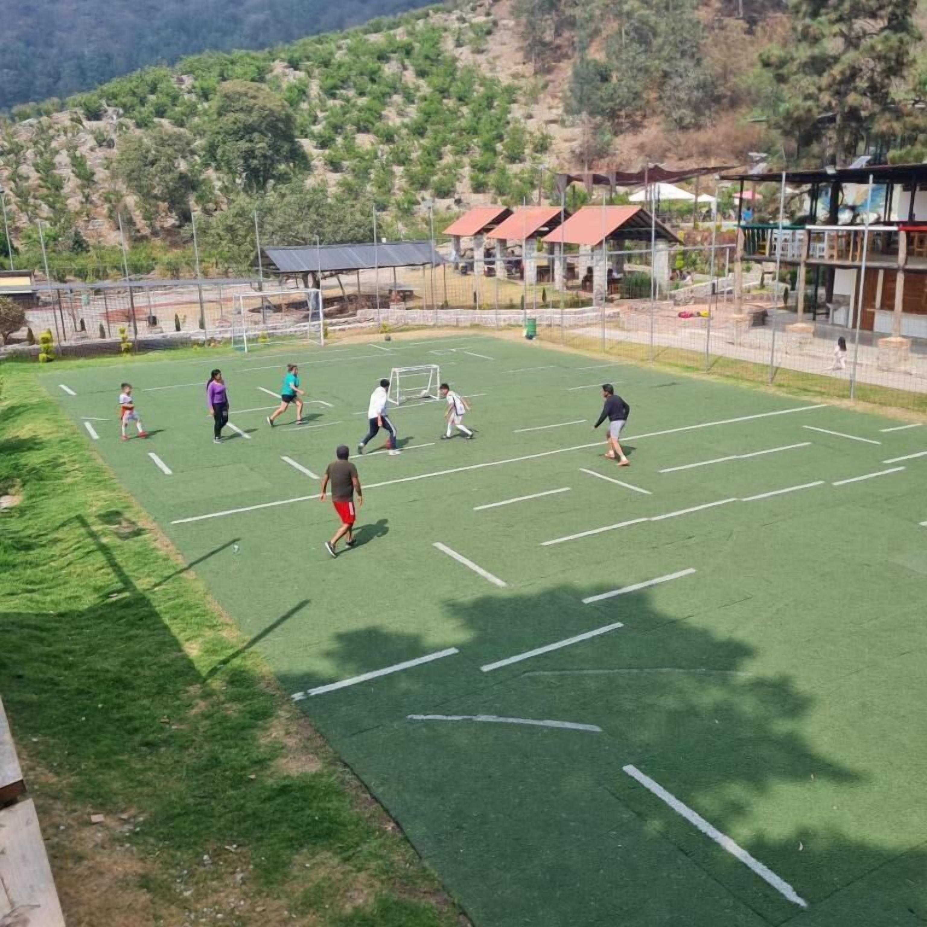 Un campo deportivo al aire libre con un arco, rodeado de una cerca y edificios al fondo.