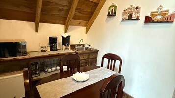 A cozy kitchen with wooden beams, a dining table with chairs, a coffee maker, and decorative wall art.