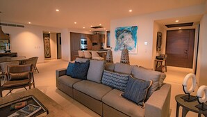 A modern living room with a grey sofa, a coffee table, and a dining area in the background.