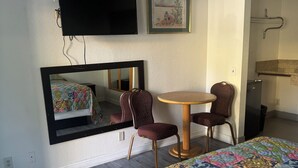 A hotel room with a bed, two chairs, a small table, a TV mounted on the wall, and a framed picture. - All 8 Motel (Azusa)