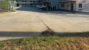 A motel with a parking lot, a fenced area, and a building with a balcony. - All 8 Motel (Azusa)