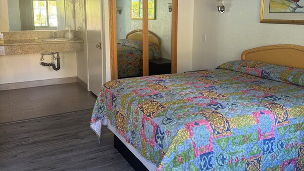 A bedroom with a bed, a bathroom with a sink, and a mirror. - All 8 Motel (Azusa)