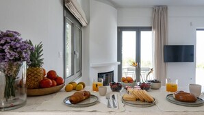A breakfast setup with fruits, pastries, and beverages on a table in a modern room with a fireplace and a TV. - Morea Club West House with Private Heated Pool (Kalamat)