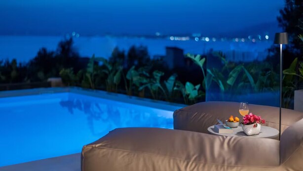 A poolside lounge with a view of the ocean, a glass table with a drink, and a bowl of fruit. - Morea Club West House with Private Heated Pool (Kalamat)