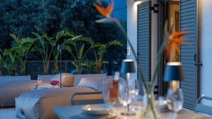 An outdoor dining area with a table set for two, surrounded by lush greenery and a comfortable seating area. - Morea Club West House with Private Heated Pool (Kalamat)