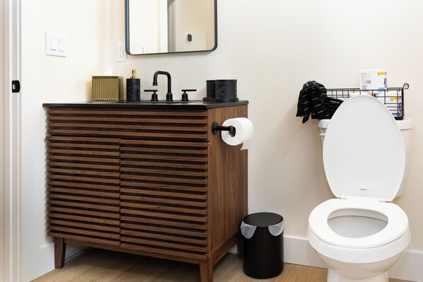 Un baño moderno con tocador de madera, inodoro blanco y cubo de basura negro.