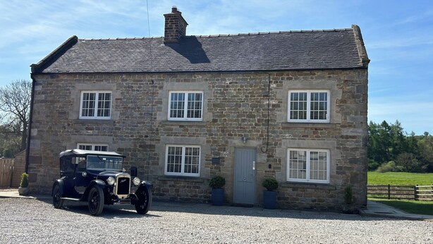 Une maison en pierre avec une voiture garée devant.