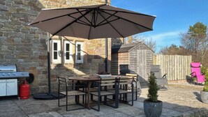 An outdoor patio with a stone table and chairs, a barbecue grill, and a large umbrella.