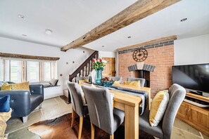 A dining area with a wooden table, grey upholstered chairs, and a brick fireplace. - Stunning Cosy Rustic Farmhouse Alton Towers Peaks (Leek)