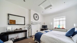 Une chambre d’hôtel équipée d’un lit, d’un bureau, d’un miroir, d’une horloge murale, d’une télévision et d’une fenêtre avec des stores.