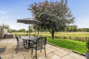A patio with a table and chairs, an umbrella, and a view of a grassy field and trees. - Stunning Cosy Rustic Farmhouse Alton Towers Peaks (Leek)