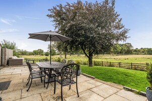 A patio with a table and chairs, an umbrella, and a view of a grassy field and trees.
