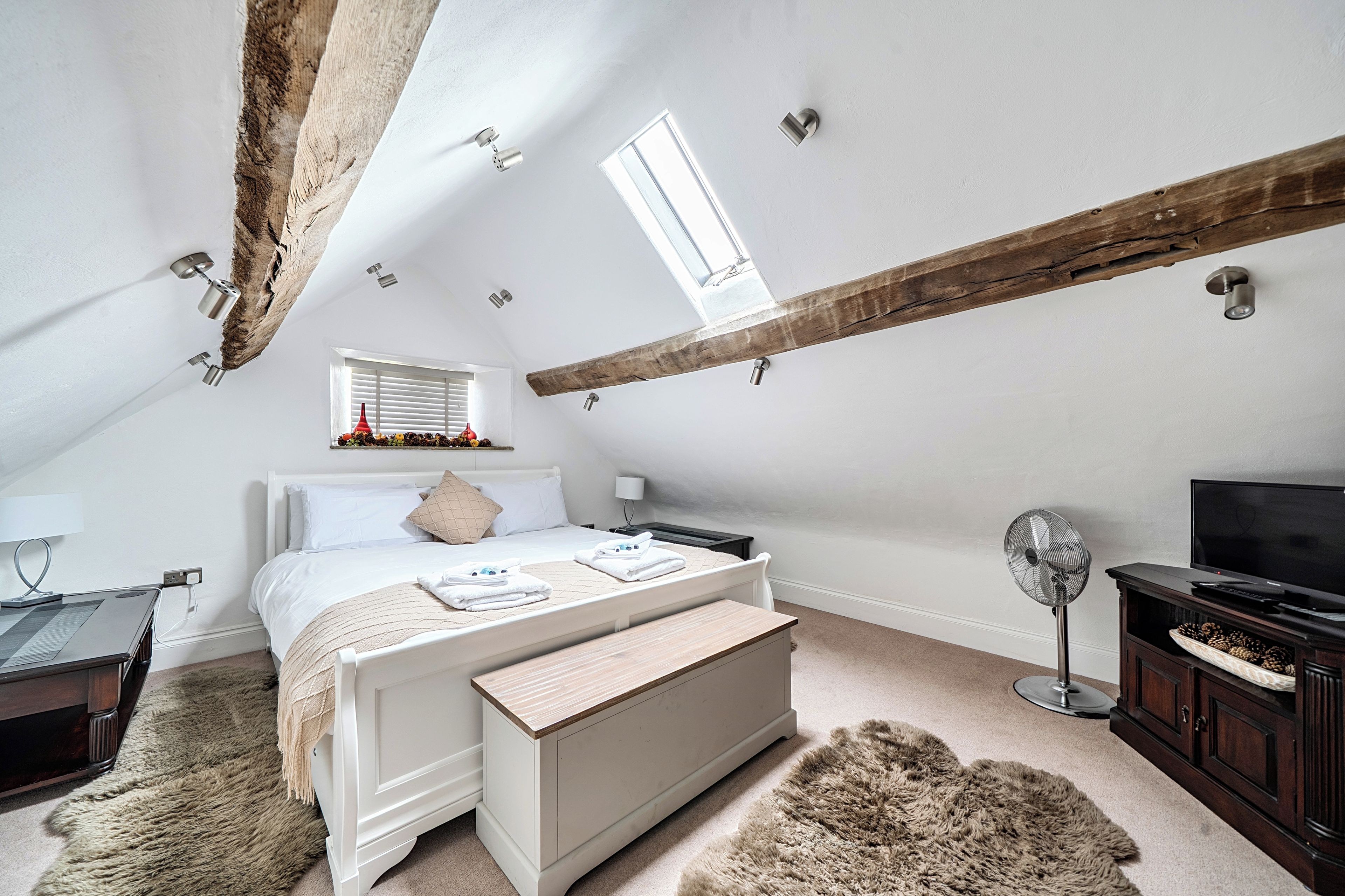 Une chambre avec un plafond en pente, un lit, un bureau, une télévision et un ventilateur.
