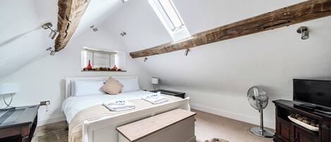 Une chambre avec un plafond en pente, un lit, un bureau, une télévision et un ventilateur.