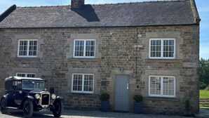 A stone building with a pitched roof, multiple windows, and a vintage car parked in front.