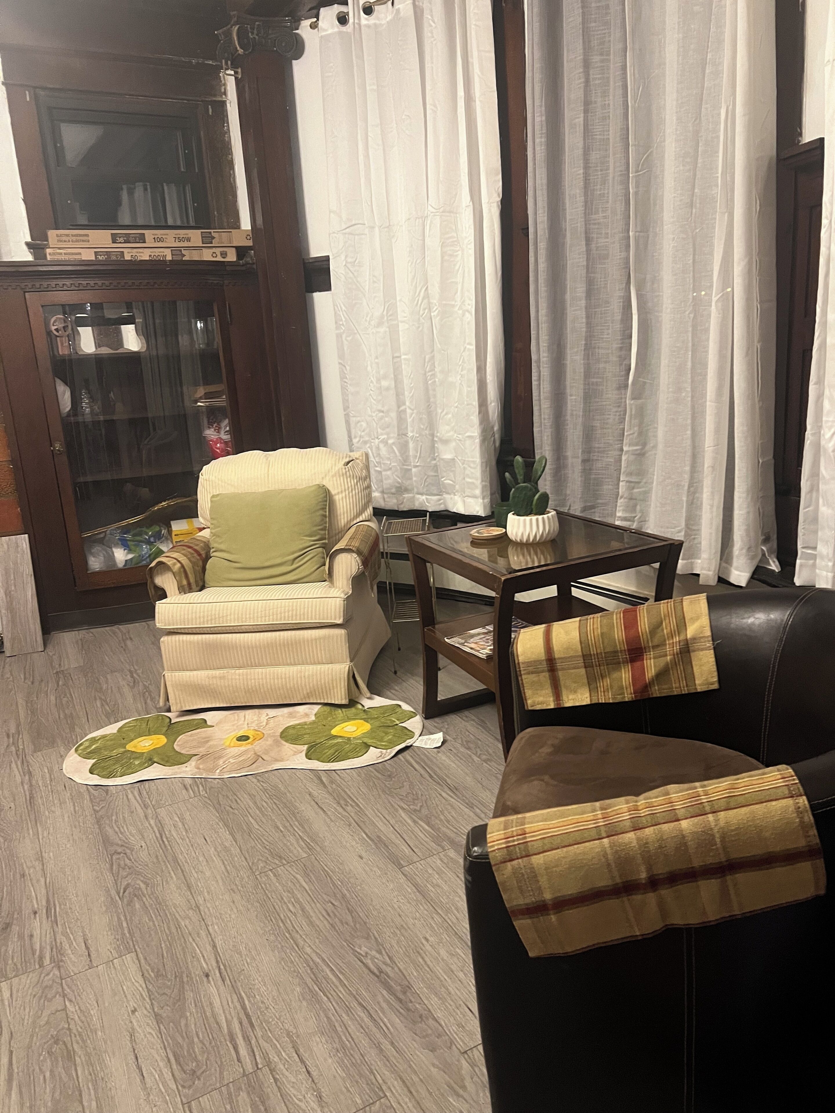 Una sala de estar con un sillón color beige, un sofá de cuero negro, una mesa de centro de madera y un aparador de vidrio.