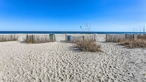 Une plage de sable bordée d’une clôture en bois, sous un ciel bleu et dégagé.