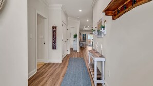 Un couloir avec un plancher en bois, un tapis bleu, une console blanche et une pancarte indiquant « BIENVENUE ».
