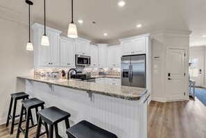 A modern kitchen with white cabinetry, a granite countertop, stainless steel appliances, and bar stools. - Blue Haven on Hallandale (Murrells Inlet)