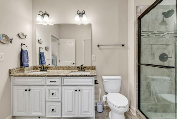 A bathroom with a double sink vanity, a toilet, and a glass shower enclosure. - Blue Haven on Hallandale (Murrells Inlet)