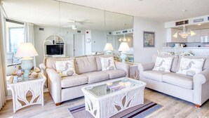 Ein Wohnzimmer mit zwei Sofas, einem Couchtisch und einem Fernseher. An einer Wand befindet sich ein großer Spiegel und eine Deckenleuchte.